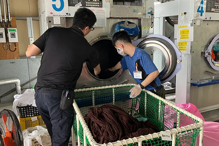 ふたりで洗濯ものを大型ドラム洗濯機に入れている写真