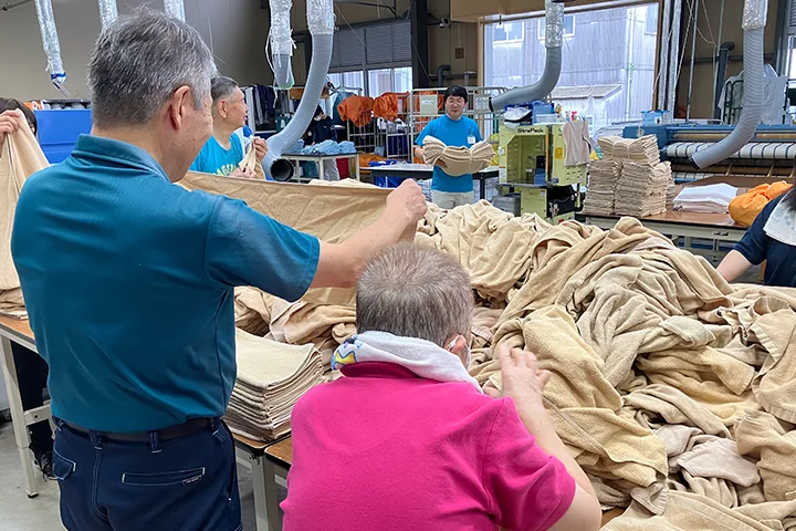 大量のタオルを数人で折りたたんでいる写真