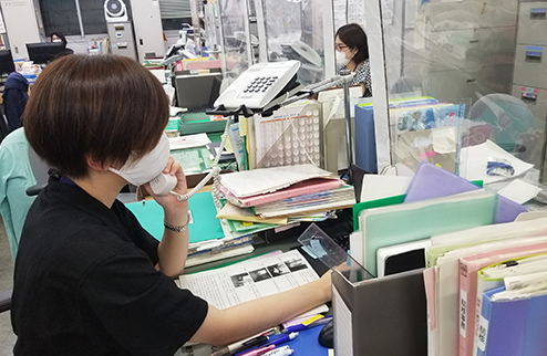 オフィス内で電話をとっている風景写真(人は皆、マスクをつけている)。